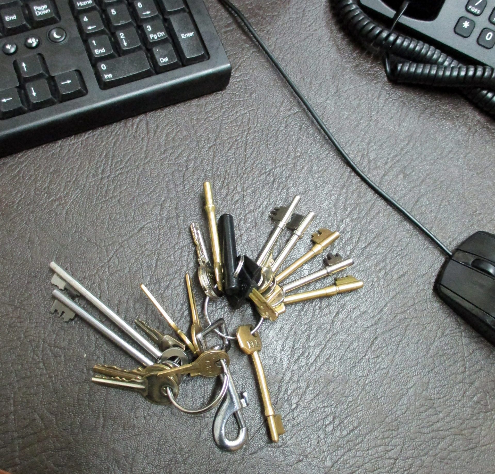 A large bunch of keys on a desk with a keyboard, phone, and mouse in the background.