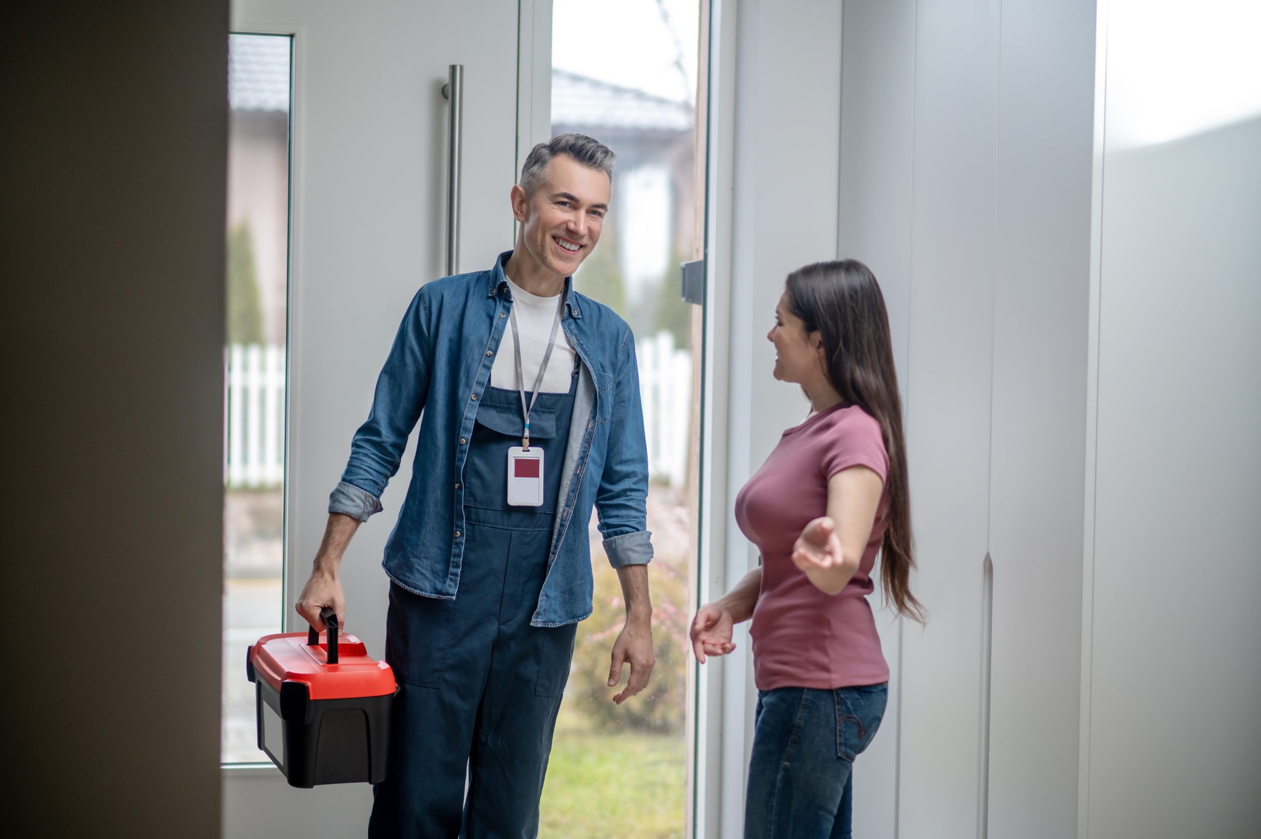 Two people walking together down a bright office corridor, with the man carrying a red toolbox and wearing a work badge.